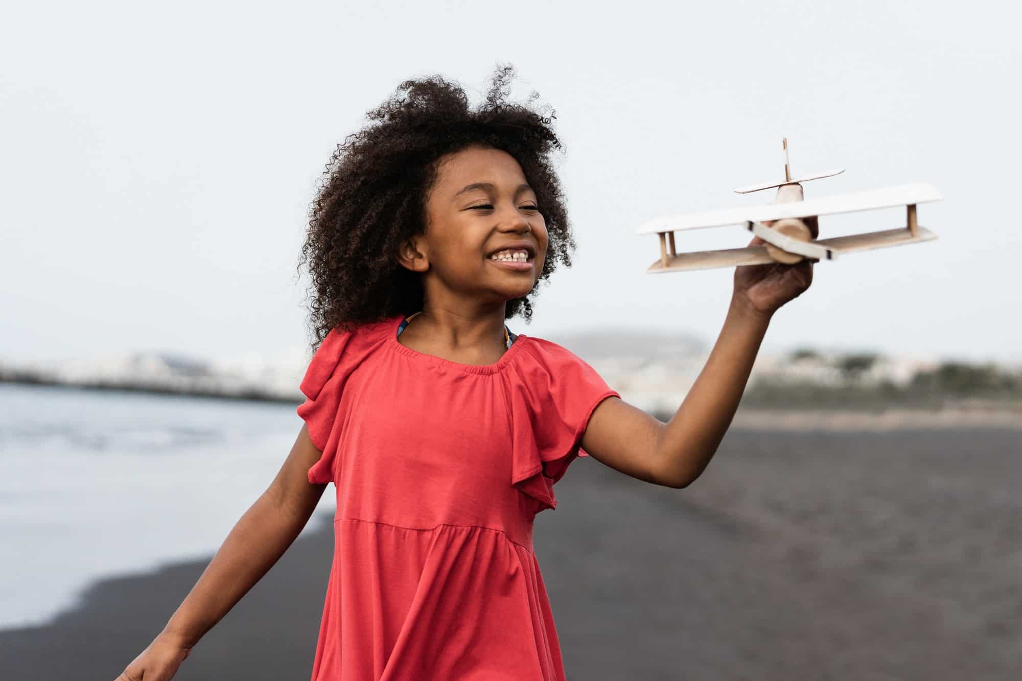 african-kid-running-on-the-beach-while-playing-with-wood-toy-airplane-focus-on-face.jpg